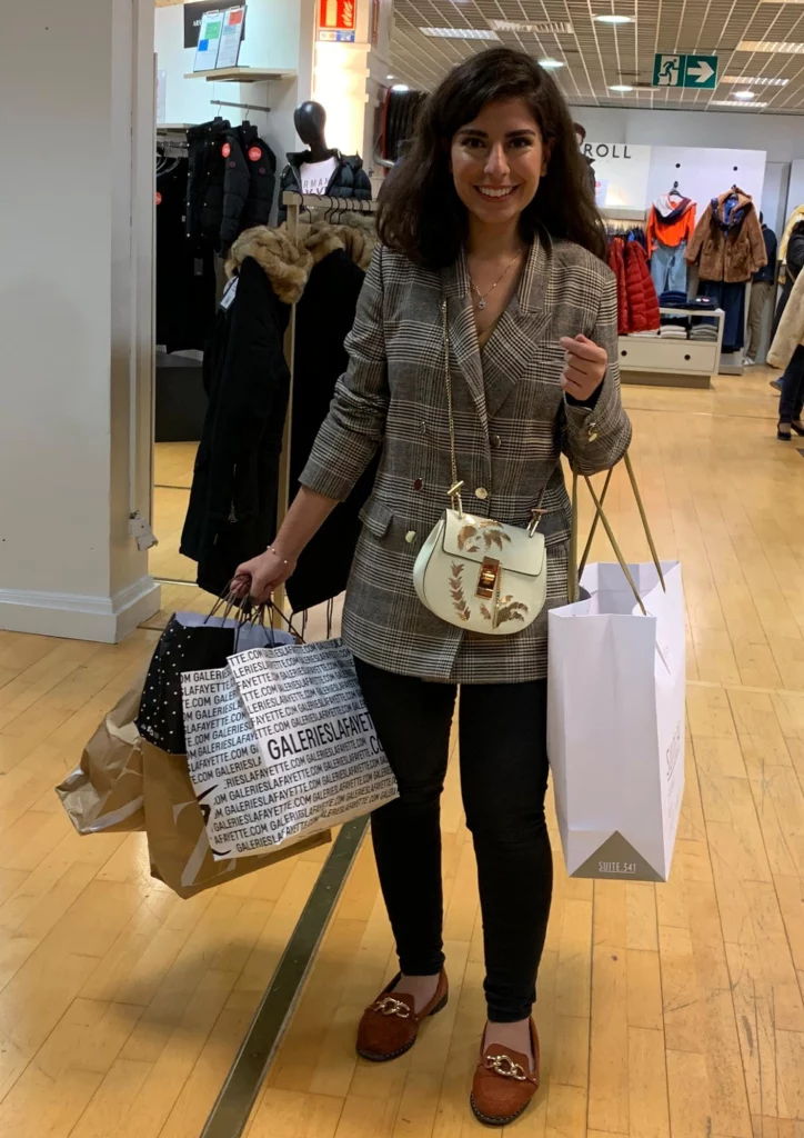 Dana personal shopper privé pour une cliente qui n'a pas le temps de faire du shopping. Dana est dans une boutique avec 4 sacs shopping.