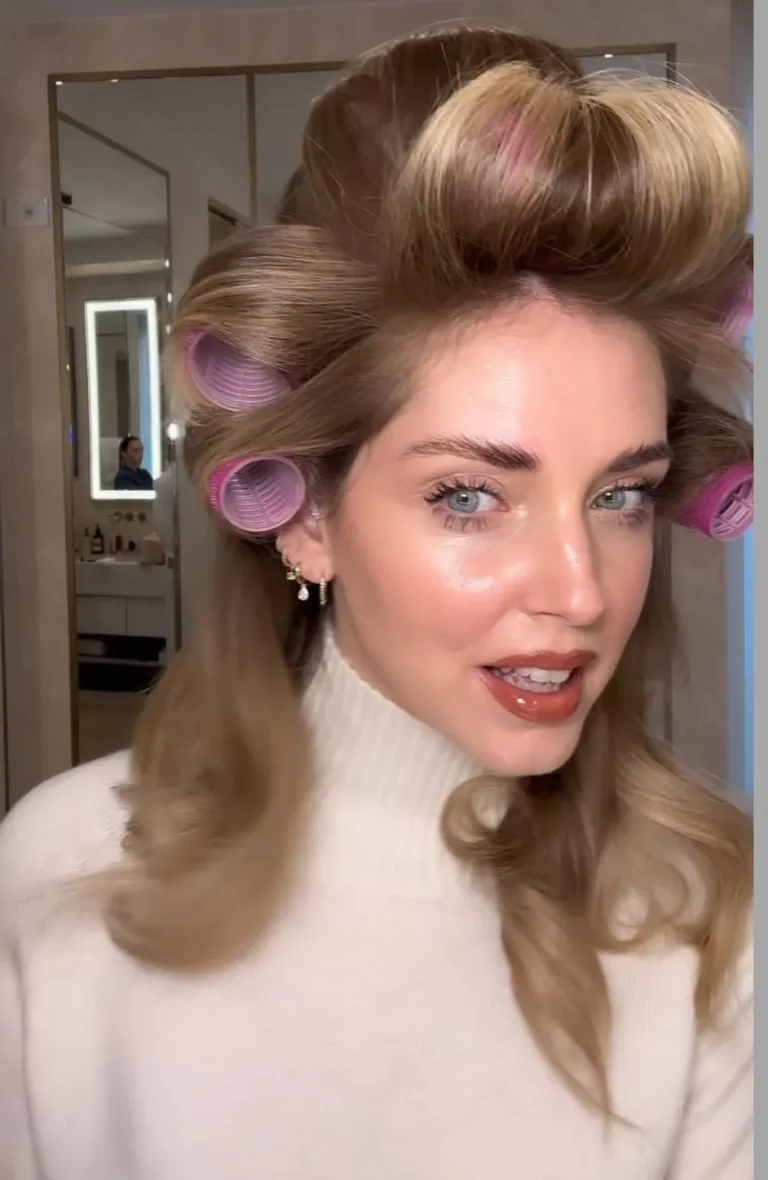 Chiara Ferragni avec des cheveux blonds coiffés de rouleaux roses et un maquillage naturel mettant en valeur ses yeux bleus, dans une ambiance élégante.