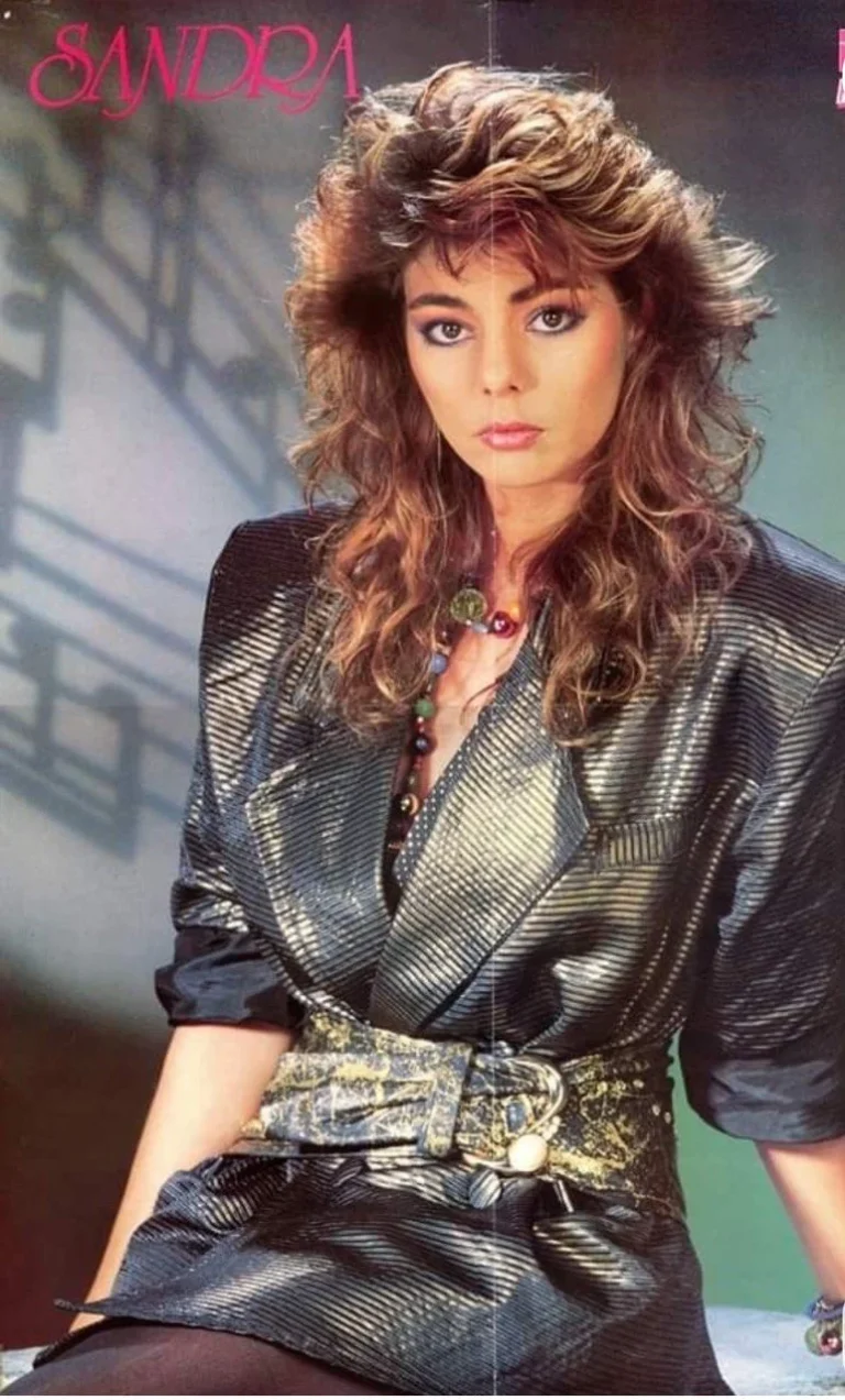 Portrait de femme aux cheveux bouclés et maquillage appuyé, vêtue d'une tenue à motifs et textures contrastées caractéristiques des années 80