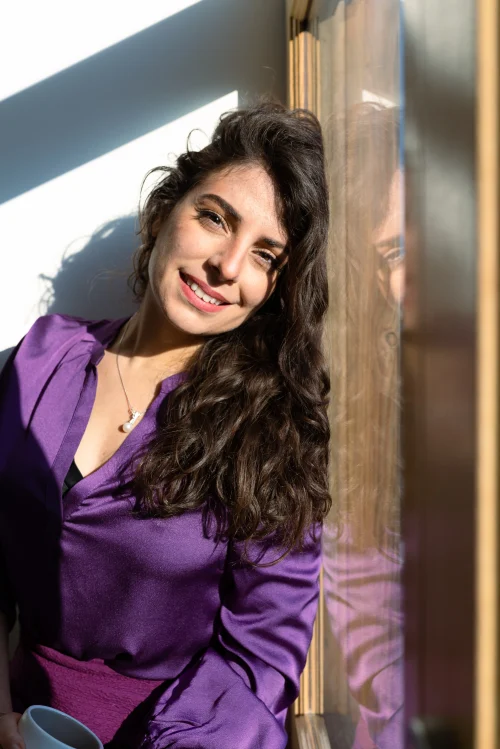 Dana, votre coach en image Dana, souriant en chemise violette, reposant sa tête sur la fenêtre